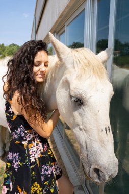 Güneşli bir günde beyaz atı kucaklayan bir kadın.