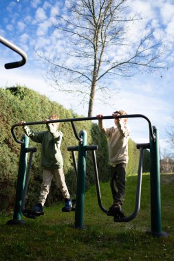 Parkta spor aletleriyle spor yapan iki genç çocuk sağlıklı yaşam tarzlarını ve açık hava aktivitelerini destekliyor.