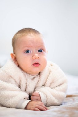 Karnının üstüne uzanmış şirin bir bebek, hoş bir yün giysi giyiyor, tuhaf bir ifadesi var.