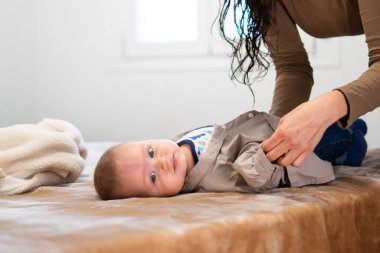 Annesi güzel bebeğini yatağa giydirip gömlek giydiriyor.
