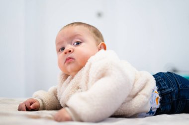 Yumuşak bir battaniyeye uzanmış sevimli bir bebek, meraklı görünüyor.