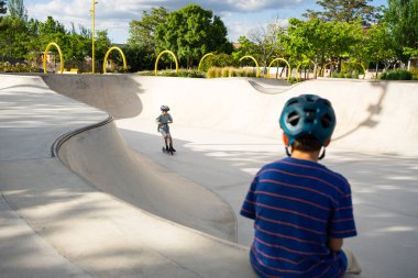 İki çocuk kaykay parkında motosiklete biniyor, açık havada yaz gününün tadını çıkarıyorlar.