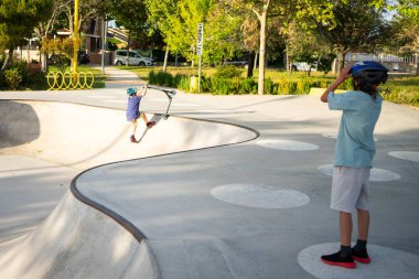 İki çocuk kaykay parkında motosiklet sürmekten zevk alıyor, numaralar yapıyor ve dışarıda eğleniyorlar.