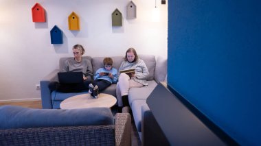 Aile bir kanepeye oturur, her insan kendi dijital cihazına kendini kaptırır.