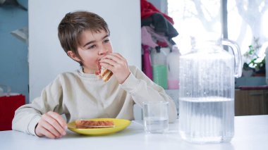 Çocuk sağlıklı bir şeyler atıştırıyor veya mutfak masasında yemek yiyor.