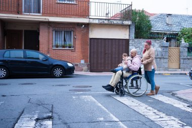 Bir şehir caddesi yaya geçidinde gezinen aile, erişilebilirliği ve dahil edilmeyi vurguluyor