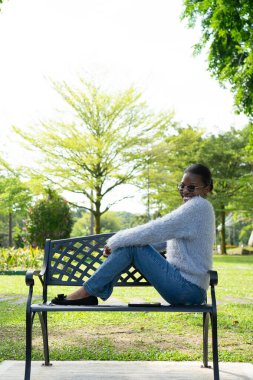 Parktaki bankta oturan genç siyahi kadın güneşli bir günün tadını çıkarıyor.