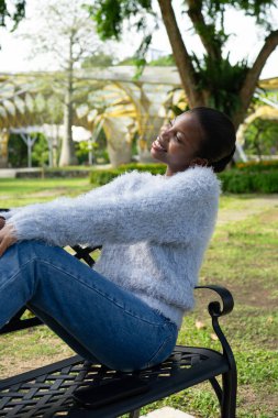 Gözleri kapalı genç bir kadın parktaki bankta dinleniyor. Huzurlu bir şehir parkında güneşin ve temiz havanın tadını çıkarıyor.