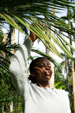 Tropik ormanda palmiye yapraklarına dokunan genç bir kadın güneş ışığının tadını çıkarıyor.