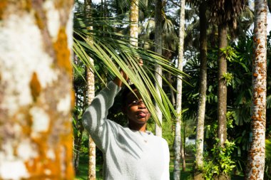 Turist, tropikal ormanlarda egzotik doğanın tadını çıkarıyor. Yüzüne palmiye yaprağı tutuyor.