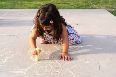 Açık hava oyun saatinde beton üzerine tebeşirle sanat yapan çocuk