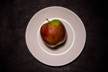 Siyah arka planda beyaz bir tabakta elma.