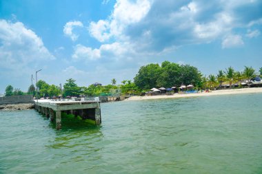 Ahşap, beton iskele, ağaçlar ve kumsal şemsiyeleri reklamcılık için açık mavi bulutlu gökyüzünün altında beyaz kum boyunca uzanır.,