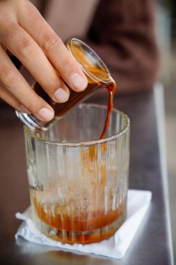 Bir kadın buz küpleriyle dolu bir bardağa altın kremayla güçlü bir espresso döktüğü an. İçi buz dolu bir bardağa dökülen kahvenin yakın çekimi..