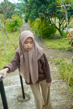Asyalı yorgun bir Müslüman kadının yeşil yapraklarla çevrili bir yolda dikilirken demir parmaklıkları sımsıkı tutuşu görüntüsü..