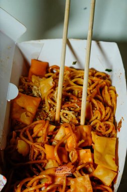 Kızarmış mantı ve bir çift yemek çubuğuyla birlikte servis edilen bir paket servis kutusunda servis edilen kızarmış eriştenin bir kısmı..