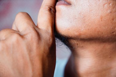A couple sits on the bed with their backs to each other. A man demonstrates a finger gesture in front of his lips which symbolizes an instruction to be quiet or keep a secret.