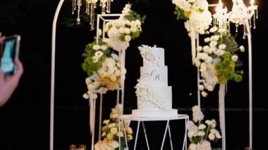 Akşam düğün kemeri beyaz çiçekler ve açık havada fenerlerle yeşillik. Resmî törende çiçek ve dekor. Kremalı büyük beyaz pasta.