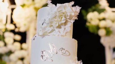 Akşam düğün kemeri beyaz çiçekler ve açık havada fenerlerle yeşillik. Resmî törende çiçek ve dekor. Kremalı büyük beyaz pasta.