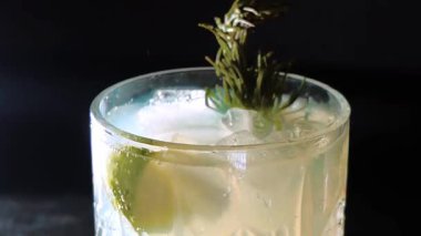 Cin tonik ve bardaklarda buzla yapılan nefis alkollü kokteyl geceleri dinlenmek ve yazın ferahlatıcı olmak için. Baharat ve aroma için yeşil limon. Barmen ve bar. Biberiye ateşle yanıyor.