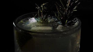 Cin tonik ve bardaklarda buzla yapılan nefis alkollü kokteyl geceleri dinlenmek ve yazın ferahlatıcı olmak için. Baharat ve aroma için yeşil limon. Barmen ve bar. Biberiye ateşle yanıyor.