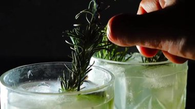 Cin tonik ve bardaklarda buzla yapılan nefis alkollü kokteyl geceleri dinlenmek ve yazın ferahlatıcı olmak için. Baharat ve aroma için yeşil limon. Barmen ve bar. Biberiye ateşle yanıyor.