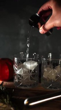 Cin tonik ve bardaklarda buzla yapılan nefis alkollü kokteyl geceleri dinlenmek ve yazın ferahlatıcı olmak için. Baharat ve aroma için yeşil limon. Barmen ve bar. Biberiye ateşle yanıyor.