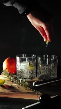 Cin tonik ve bardaklarda buzla yapılan nefis alkollü kokteyl geceleri dinlenmek ve yazın ferahlatıcı olmak için. Baharat ve aroma için yeşil limon. Barmen ve bar. Biberiye ateşle yanıyor.