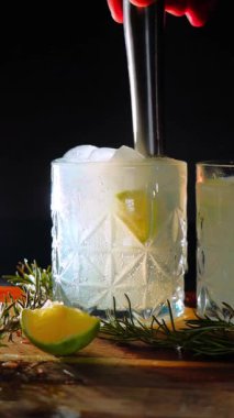 Cin tonik ve bardaklarda buzla yapılan nefis alkollü kokteyl geceleri dinlenmek ve yazın ferahlatıcı olmak için. Baharat ve aroma için yeşil limon. Barmen ve bar. Biberiye ateşle yanıyor.