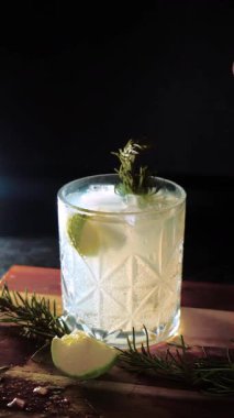 Cin tonik ve bardaklarda buzla yapılan nefis alkollü kokteyl geceleri dinlenmek ve yazın ferahlatıcı olmak için. Baharat ve aroma için yeşil limon. Barmen ve bar. Biberiye ateşle yanıyor.