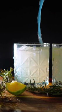 Cin tonik ve bardaklarda buzla yapılan nefis alkollü kokteyl geceleri dinlenmek ve yazın ferahlatıcı olmak için. Baharat ve aroma için yeşil limon. Barmen ve bar. Biberiye ateşle yanıyor.