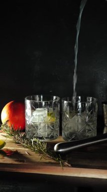 Cin tonik ve bardaklarda buzla yapılan nefis alkollü kokteyl geceleri dinlenmek ve yazın ferahlatıcı olmak için. Baharat ve aroma için yeşil limon. Barmen ve bar. Biberiye ateşle yanıyor.