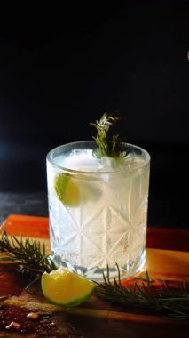 Cin tonik ve bardaklarda buzla yapılan nefis alkollü kokteyl geceleri dinlenmek ve yazın ferahlatıcı olmak için. Baharat ve aroma için yeşil limon. Barmen ve bar. Biberiye ateşle yanıyor.