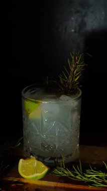 Cin tonik ve bardaklarda buzla yapılan nefis alkollü kokteyl geceleri dinlenmek ve yazın ferahlatıcı olmak için. Baharat ve aroma için yeşil limon. Barmen ve bar. Biberiye ateşle yanıyor.