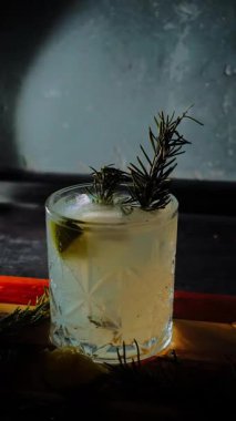 Cin tonik ve bardaklarda buzla yapılan nefis alkollü kokteyl geceleri dinlenmek ve yazın ferahlatıcı olmak için. Baharat ve aroma için yeşil limon. Barmen ve bar. Biberiye ateşle yanıyor.