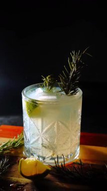 Cin tonik ve bardaklarda buzla yapılan nefis alkollü kokteyl geceleri dinlenmek ve yazın ferahlatıcı olmak için. Baharat ve aroma için yeşil limon. Barmen ve bar. Biberiye ateşle yanıyor.