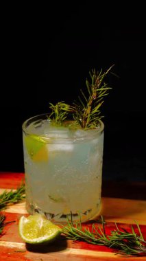 Cin tonik ve bardaklarda buzla yapılan nefis alkollü kokteyl geceleri dinlenmek ve yazın ferahlatıcı olmak için. Baharat ve aroma için yeşil limon. Barmen ve bar. Biberiye ateşle yanıyor.