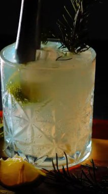 Cin tonik ve bardaklarda buzla yapılan nefis alkollü kokteyl geceleri dinlenmek ve yazın ferahlatıcı olmak için. Baharat ve aroma için yeşil limon. Barmen ve bar. Biberiye ateşle yanıyor.