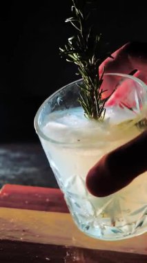 Cin tonik ve bardaklarda buzla yapılan nefis alkollü kokteyl geceleri dinlenmek ve yazın ferahlatıcı olmak için. Baharat ve aroma için yeşil limon. Barmen ve bar. Biberiye ateşle yanıyor.