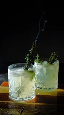 Cin tonik ve bardaklarda buzla yapılan nefis alkollü kokteyl geceleri dinlenmek ve yazın ferahlatıcı olmak için. Baharat ve aroma için yeşil limon. Barmen ve bar. Biberiye ateşle yanıyor.