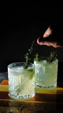 Cin tonik ve bardaklarda buzla yapılan nefis alkollü kokteyl geceleri dinlenmek ve yazın ferahlatıcı olmak için. Baharat ve aroma için yeşil limon. Barmen ve bar. Biberiye ateşle yanıyor.