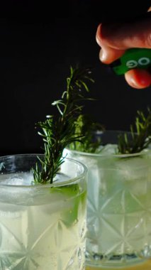 Cin tonik ve bardaklarda buzla yapılan nefis alkollü kokteyl geceleri dinlenmek ve yazın ferahlatıcı olmak için. Baharat ve aroma için yeşil limon. Barmen ve bar. Biberiye ateşle yanıyor.