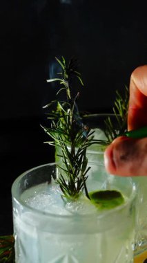 Cin tonik ve bardaklarda buzla yapılan nefis alkollü kokteyl geceleri dinlenmek ve yazın ferahlatıcı olmak için. Baharat ve aroma için yeşil limon. Barmen ve bar. Biberiye ateşle yanıyor.