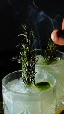 Cin tonik ve bardaklarda buzla yapılan nefis alkollü kokteyl geceleri dinlenmek ve yazın ferahlatıcı olmak için. Baharat ve aroma için yeşil limon. Barmen ve bar. Biberiye ateşle yanıyor.