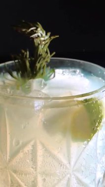 Cin tonik ve bardaklarda buzla yapılan nefis alkollü kokteyl geceleri dinlenmek ve yazın ferahlatıcı olmak için. Baharat ve aroma için yeşil limon. Barmen ve bar. Biberiye ateşle yanıyor.