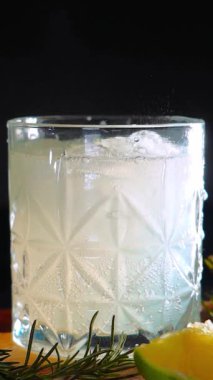 Cin tonik ve bardaklarda buzla yapılan nefis alkollü kokteyl geceleri dinlenmek ve yazın ferahlatıcı olmak için. Baharat ve aroma için yeşil limon. Barmen ve bar. Biberiye ateşle yanıyor.