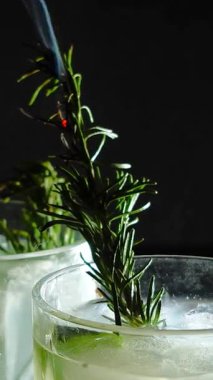 Cin tonik ve bardaklarda buzla yapılan nefis alkollü kokteyl geceleri dinlenmek ve yazın ferahlatıcı olmak için. Baharat ve aroma için yeşil limon. Barmen ve bar. Biberiye ateşle yanıyor.