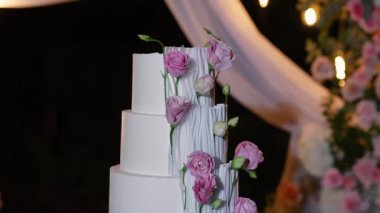 Akşam düğün kemeri beyaz çiçekler ve açık havada fenerlerle yeşillik. Resmî törende çiçek ve dekor. Kremalı büyük beyaz pasta.