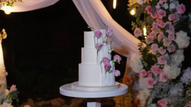 Akşam düğün kemeri beyaz çiçekler ve açık havada fenerlerle yeşillik. Resmî törende çiçek ve dekor. Kremalı büyük beyaz pasta.