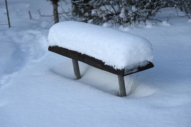 Kış parkında beyaz karla kaplı ahşap bir bank.